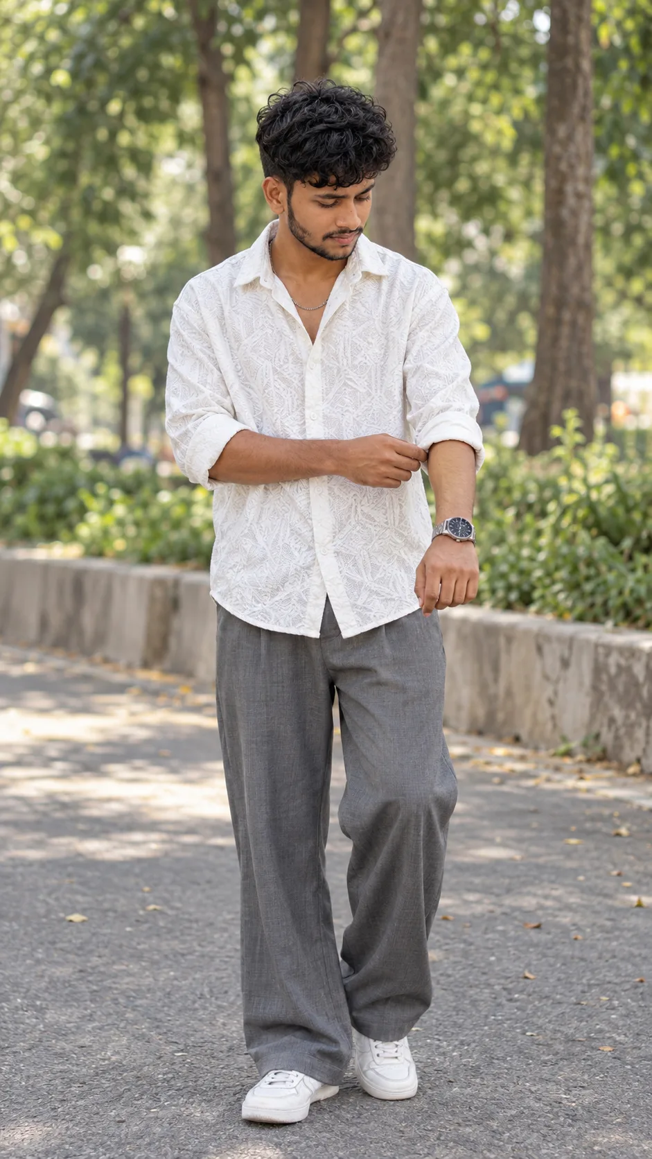 > A young man (use reference image) stands outdoors in a relaxed pose while folding the sleeve of his shirt with one hand.