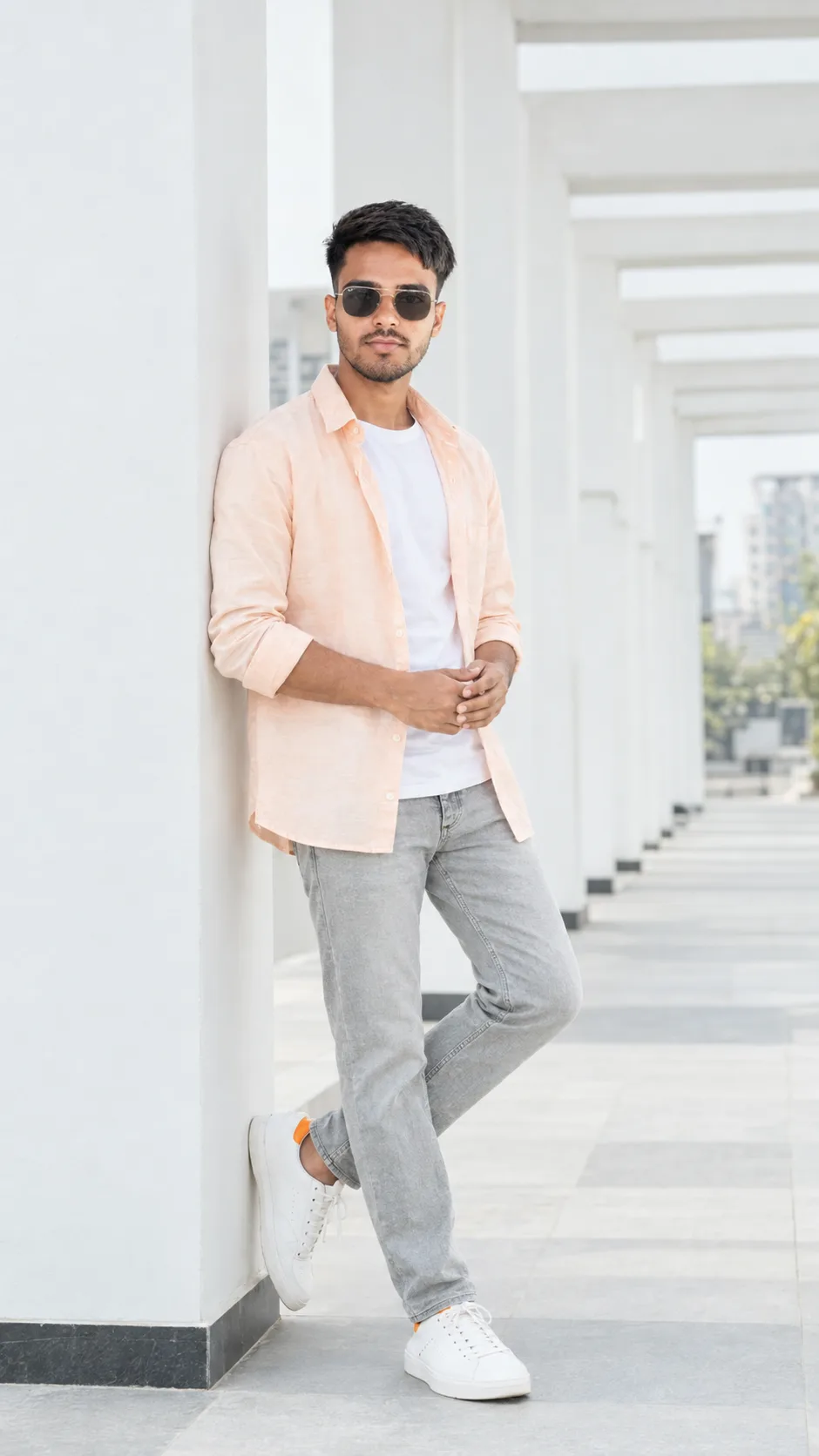 Ultra-realistic full-body fashion portrait of a handsome young Indian man standing casually against a modern white architectural wall in a