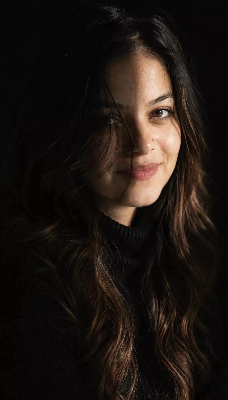 Aesthetic moody portrait of a beautiful young Indian woman in her early 20s, long wavy black hair falling on face, fair glowing natural