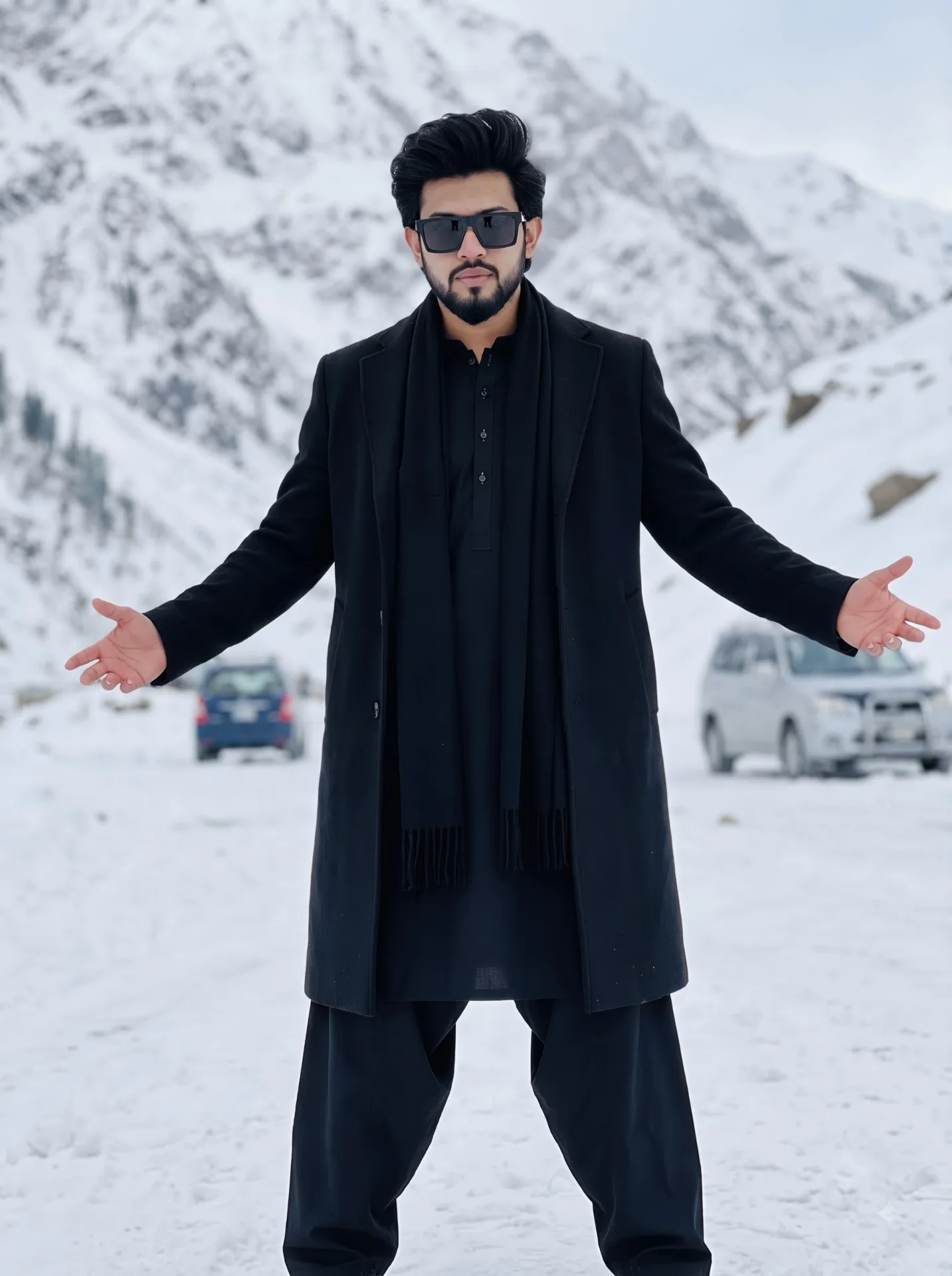 A full-body, ultra-realistic monochrome fashion portrait of a young South Asian man standing confidently in the center of a snowy mountain