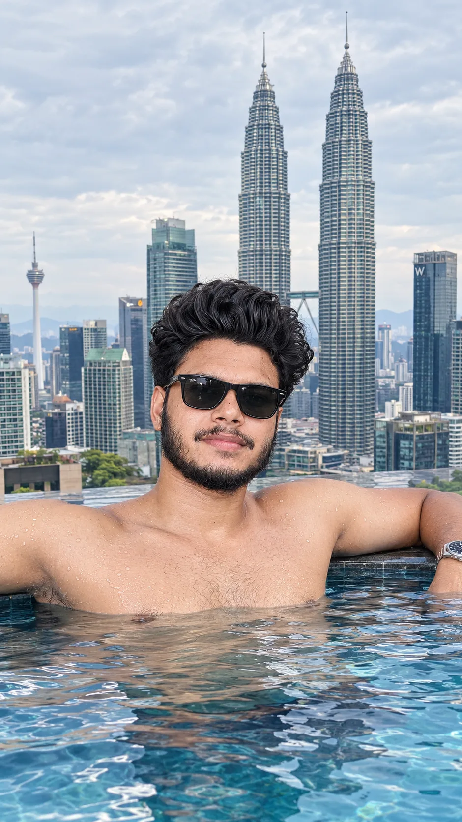 A handsome young man with dark curly hair, trimmed beard and mustache, wearing black Ray-Ban sunglasses, relaxed and shirtless in a clear