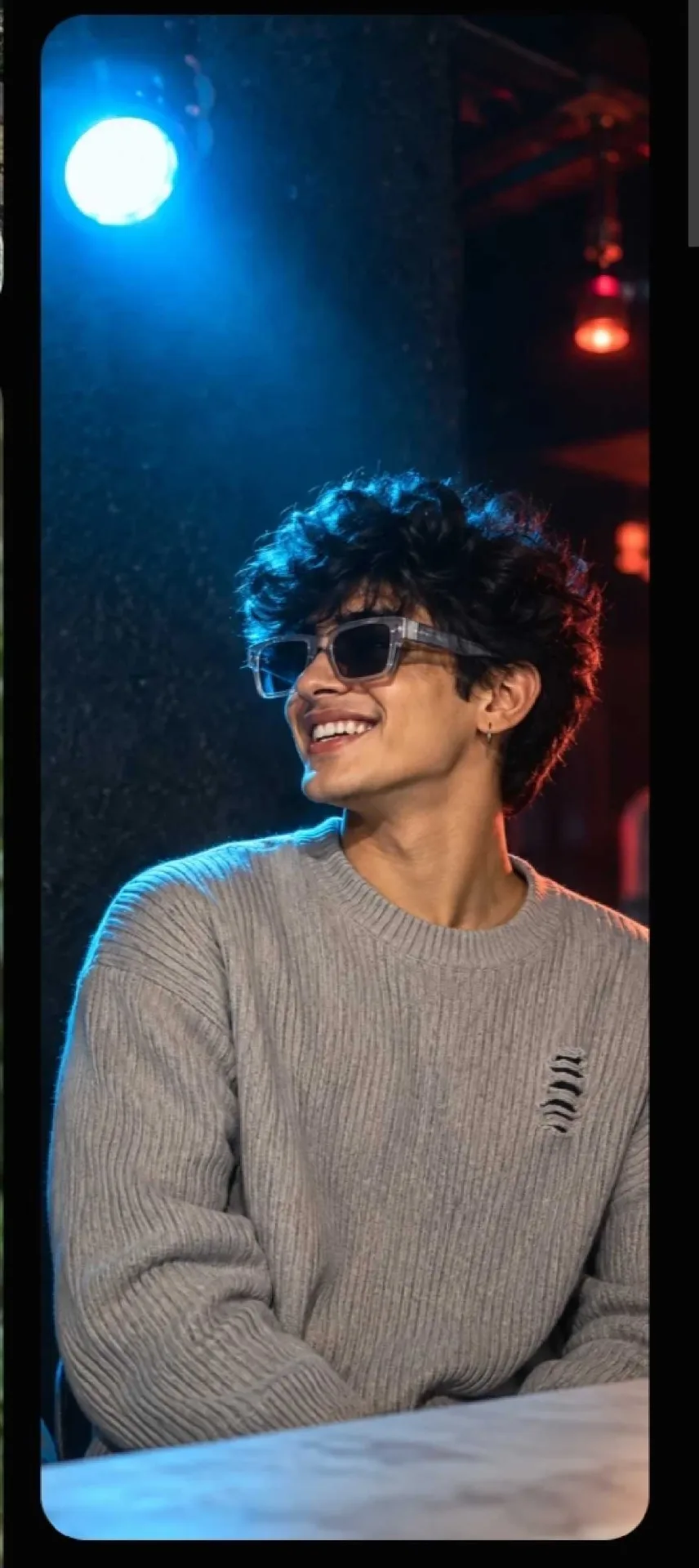 Cinematic portrait of a young Indian man with curly black hair, wearing transparent grey sunglasses and light grey ripped knit sweater,