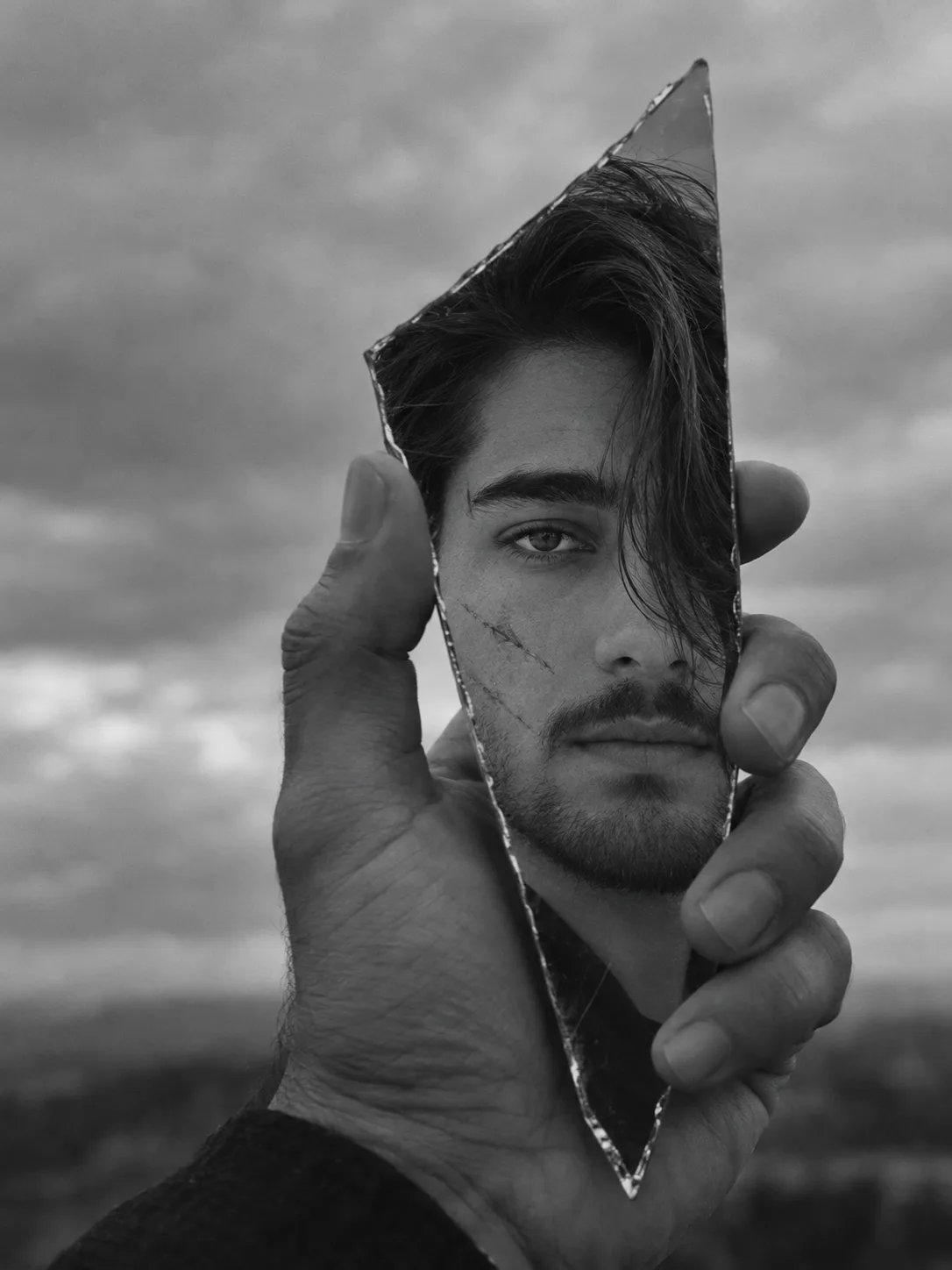 **Ultra-realistic cinematic black-and-white conceptual portrait photograph of a young adult man’s face reflected in a sharp, irregular