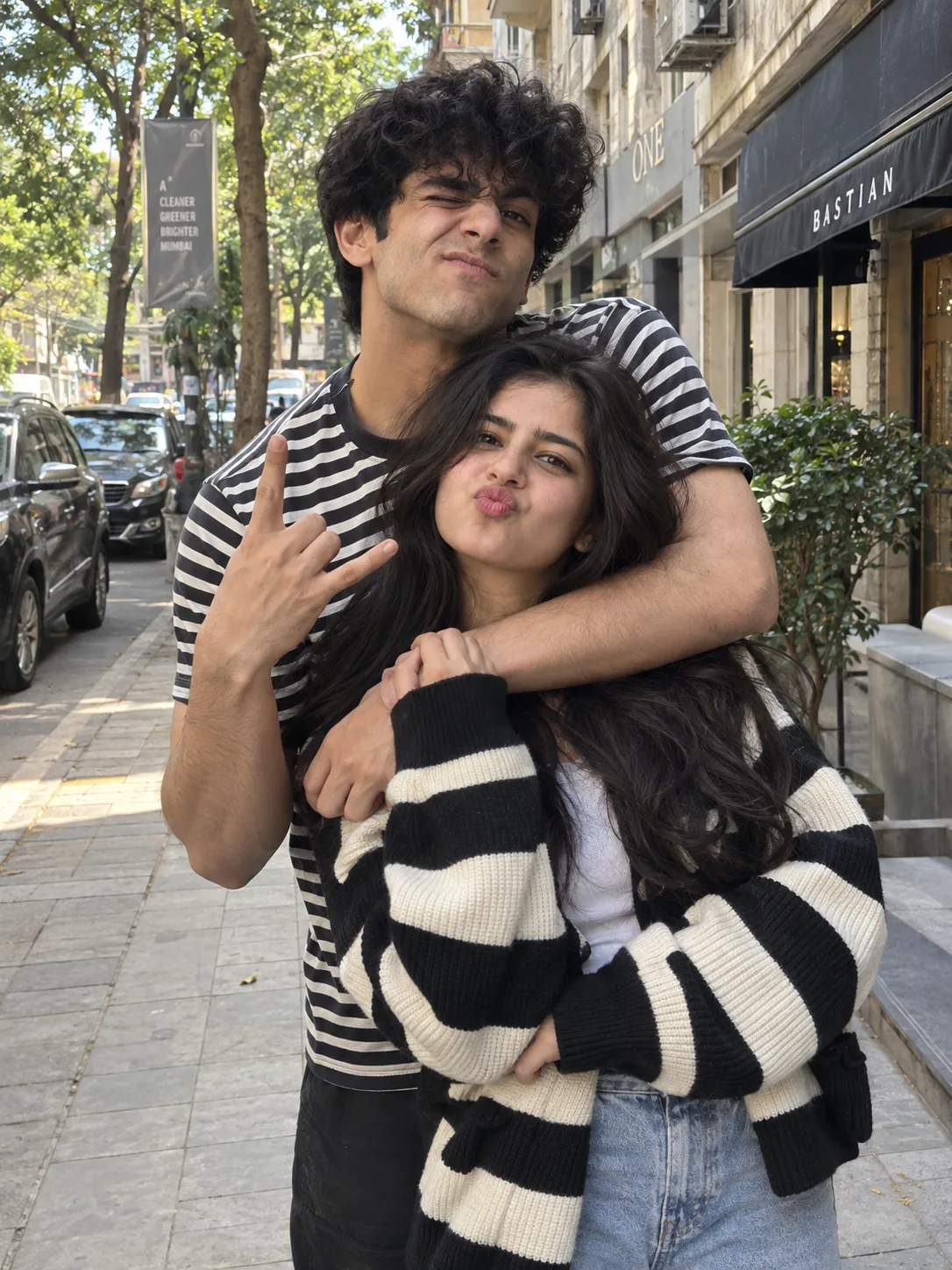 "An ultra-realistic, highly candid out door photo of a playful young South Asian couple posing funnily on a cit y sidewalk.