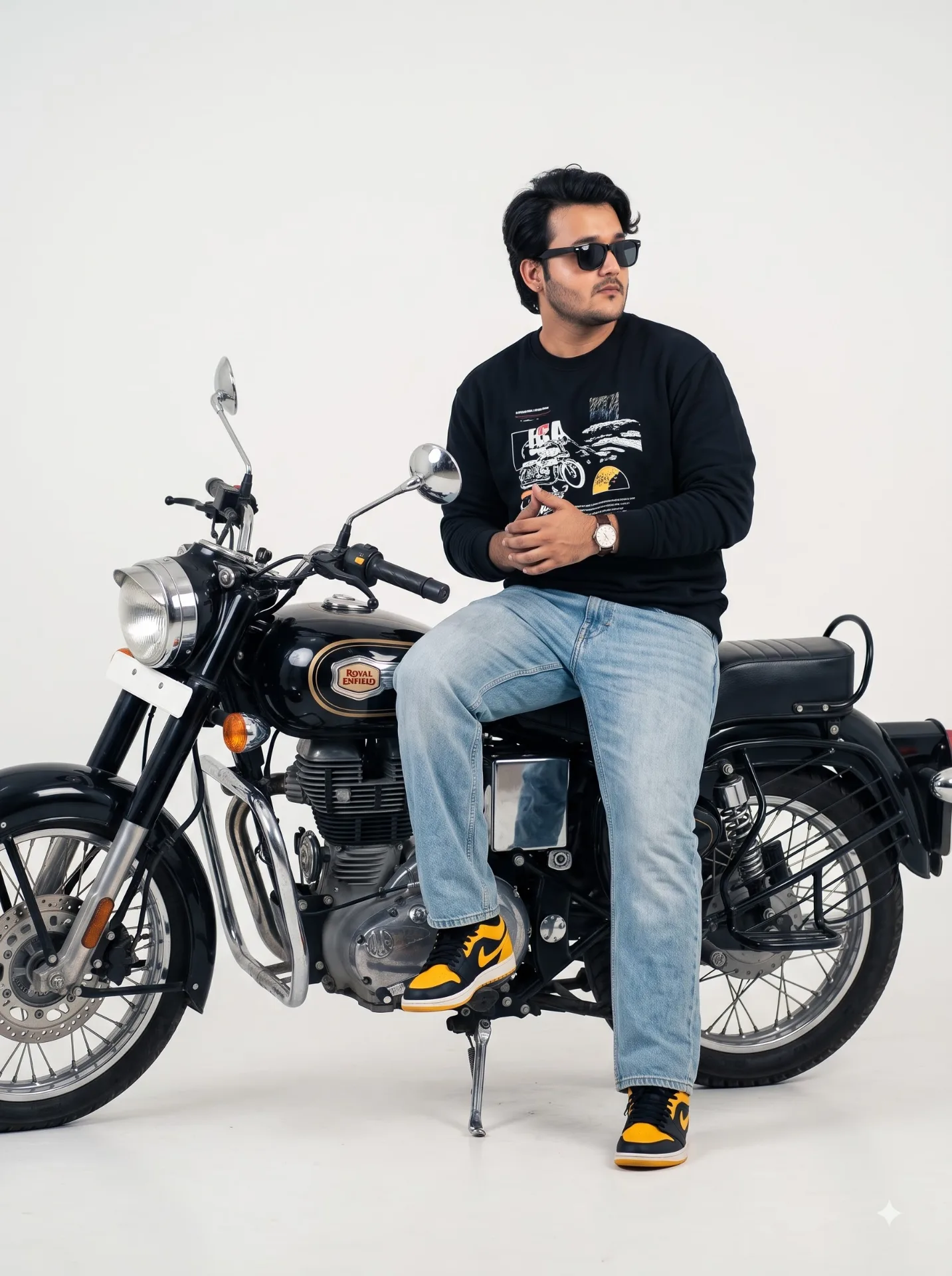 A stylish young man with curly hair, wearing black sunglasses, sitting on a black Royal Enfield-style vintage motorcycle in a minimalist