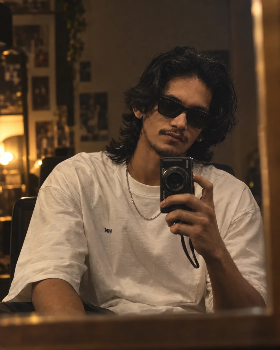 Ultra-realistic cinematic mirror selfie of a young South Asian man sitting casually in a dimly lit bedroom, captured through a large wall