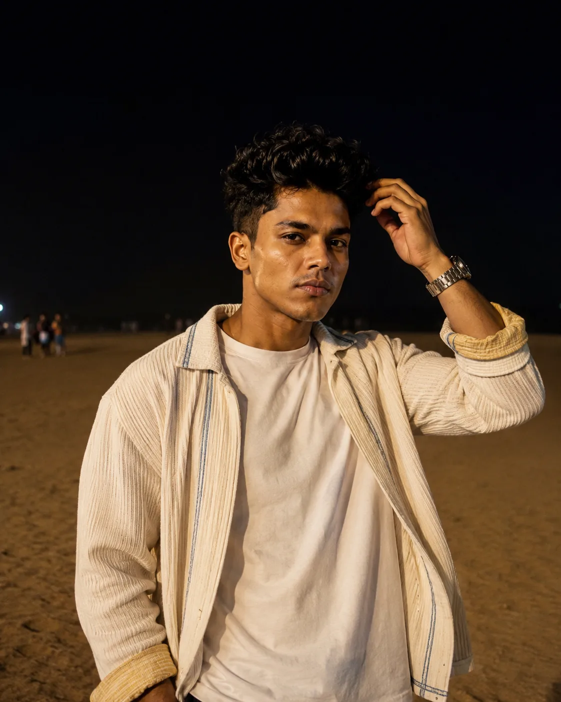 Create a realistic nighttime outdoor portrait of a young man standing on a sandy beach or open shoreline.