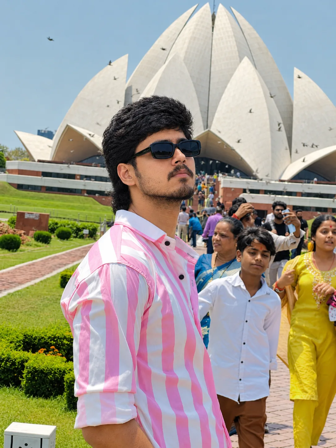 Create a photorealistic candid travel photograph of a young Indian man taking a natural outdoor portrait at the Lotus Temple in New Delhi.