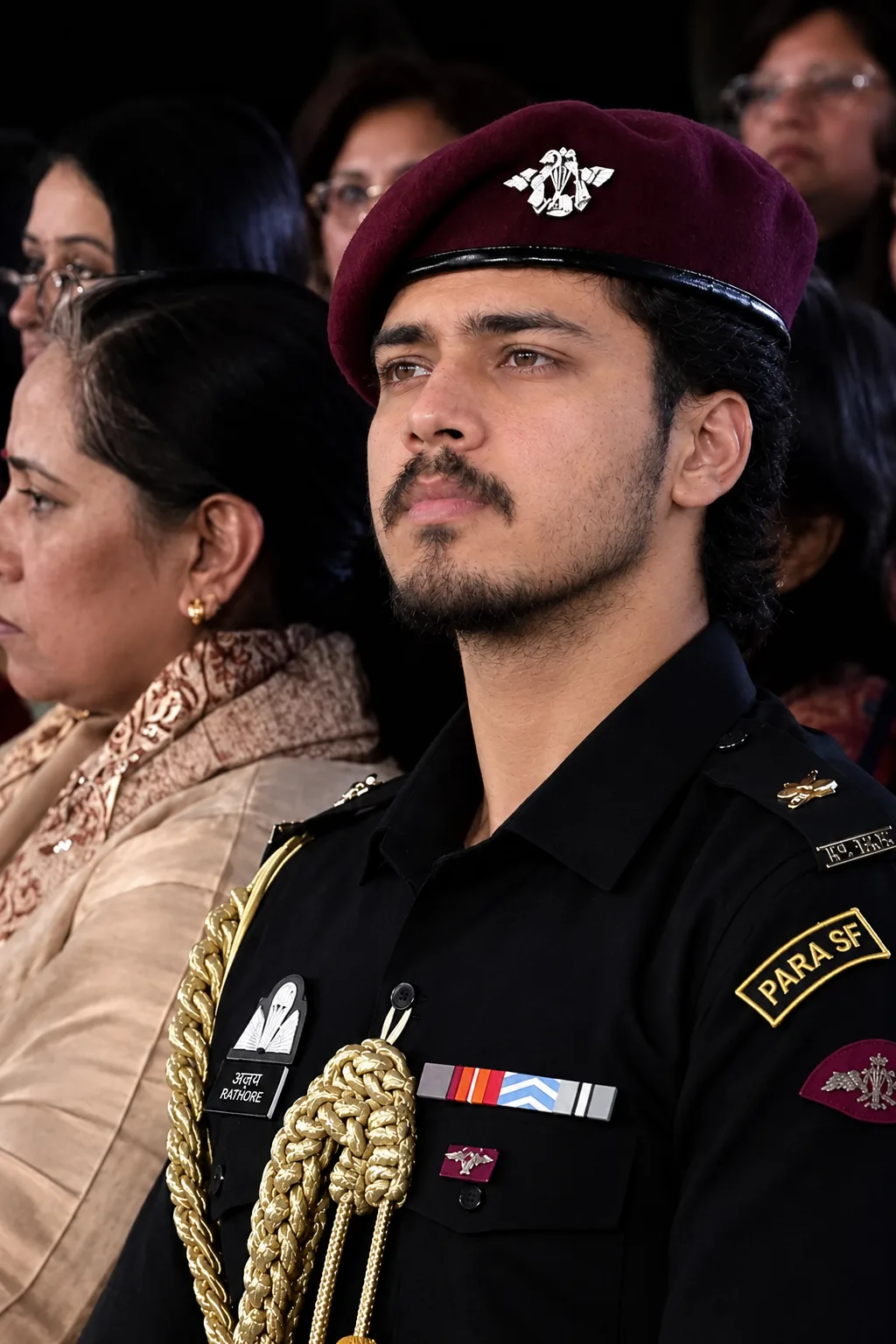 A photorealistic vertical close-up portrait of a young South Asian male officer seated at a formal military ceremony.