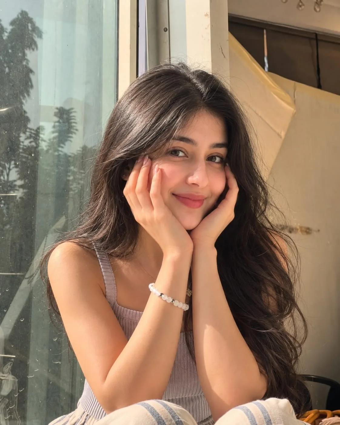 Create a realistic high-resolution portrait of a young woman sitting near a large bright window, posing with both hands gently resting