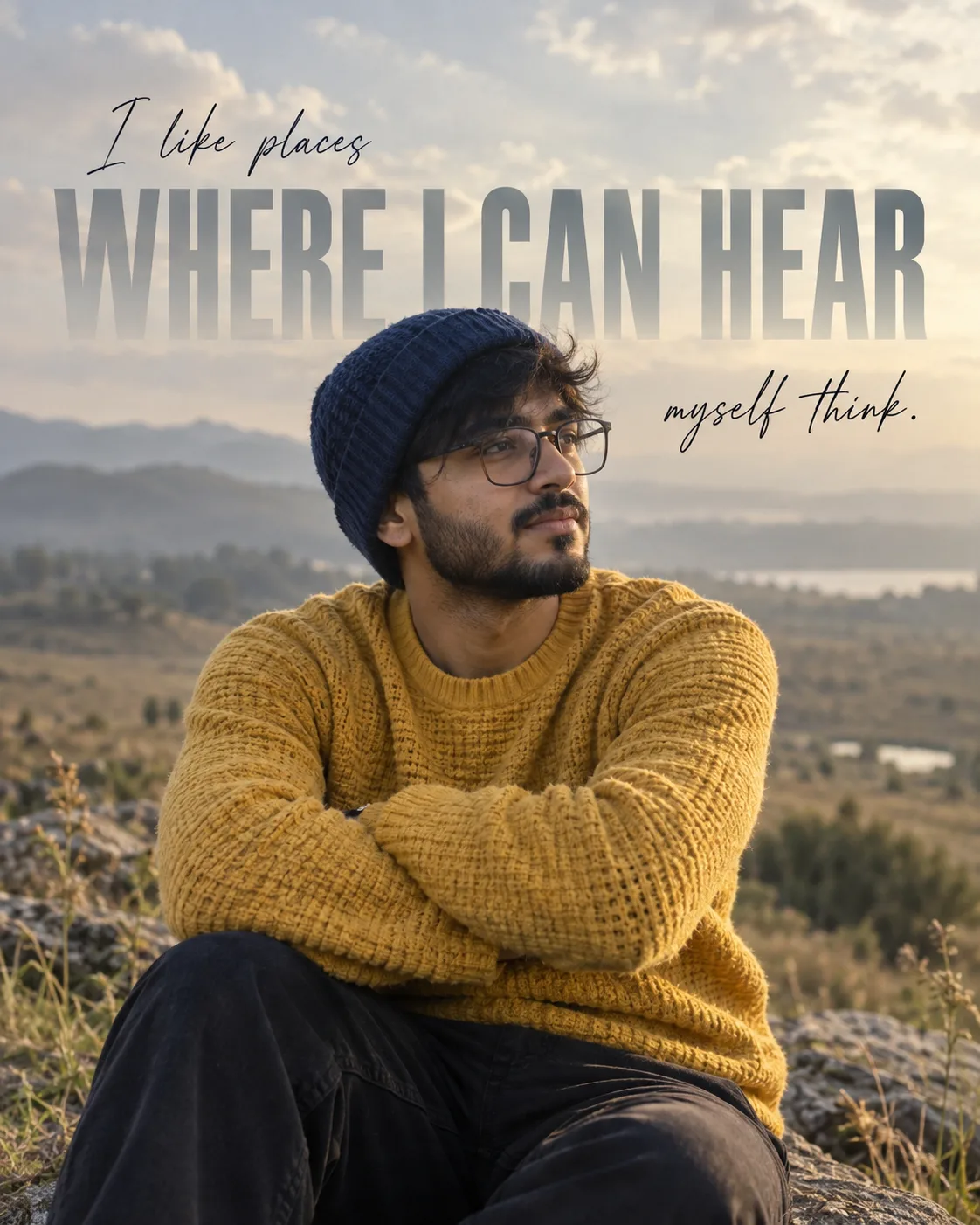 Medium shot of a YOUNG INDIAN man with glasses and beard wearing a blue beanie and textured yellow sweater, sitting with arms crossed.