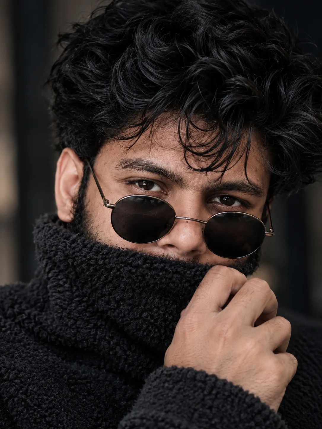 Close-up portrait of a young South Asian man with thick, voluminous, messy black curly hair falling over his forehead, intense dark brown