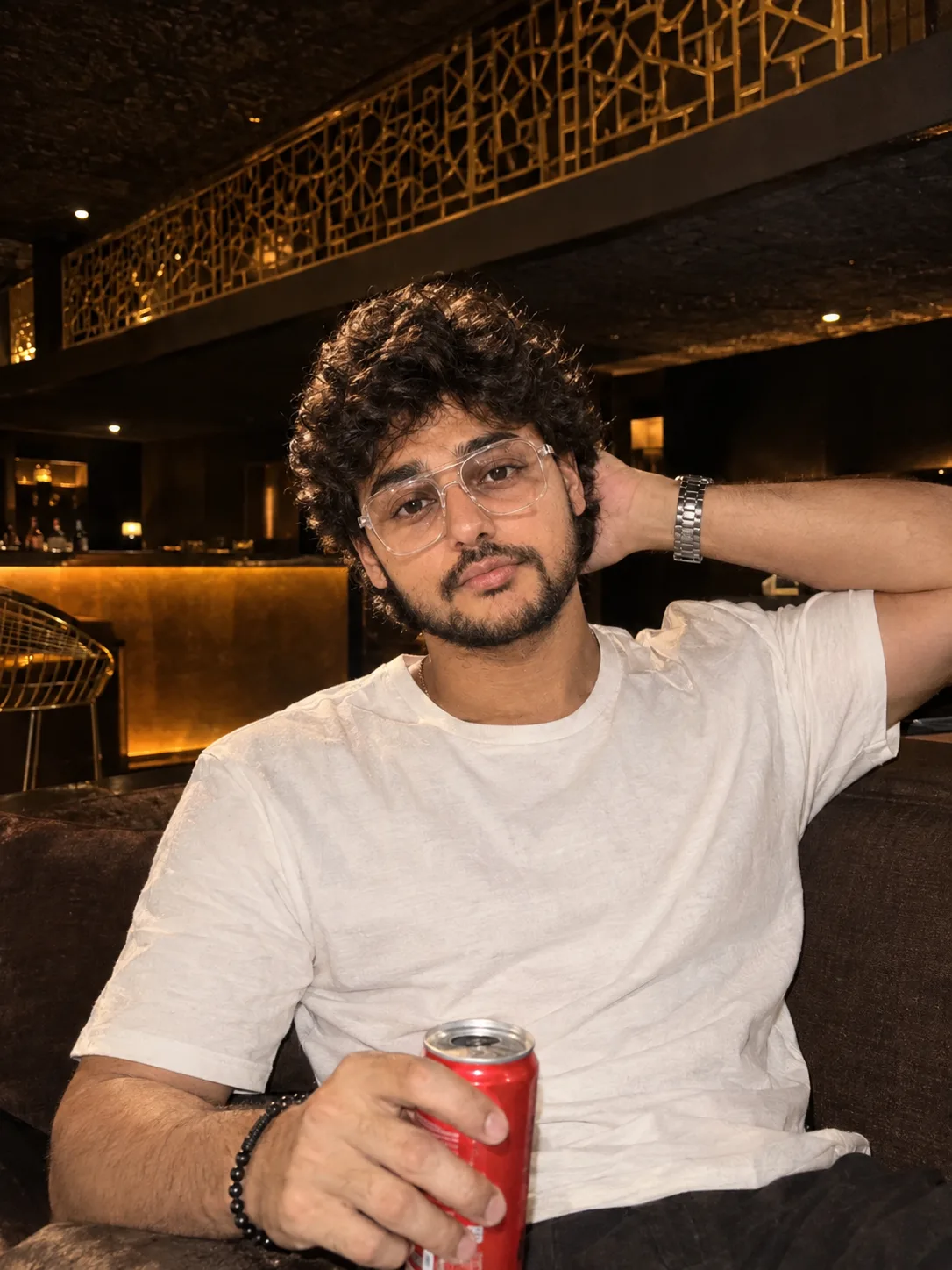"A candid, flash-lit portrait of a young man with thick, tight black curly hair and light stubble, looking at the camera with a relaxed,