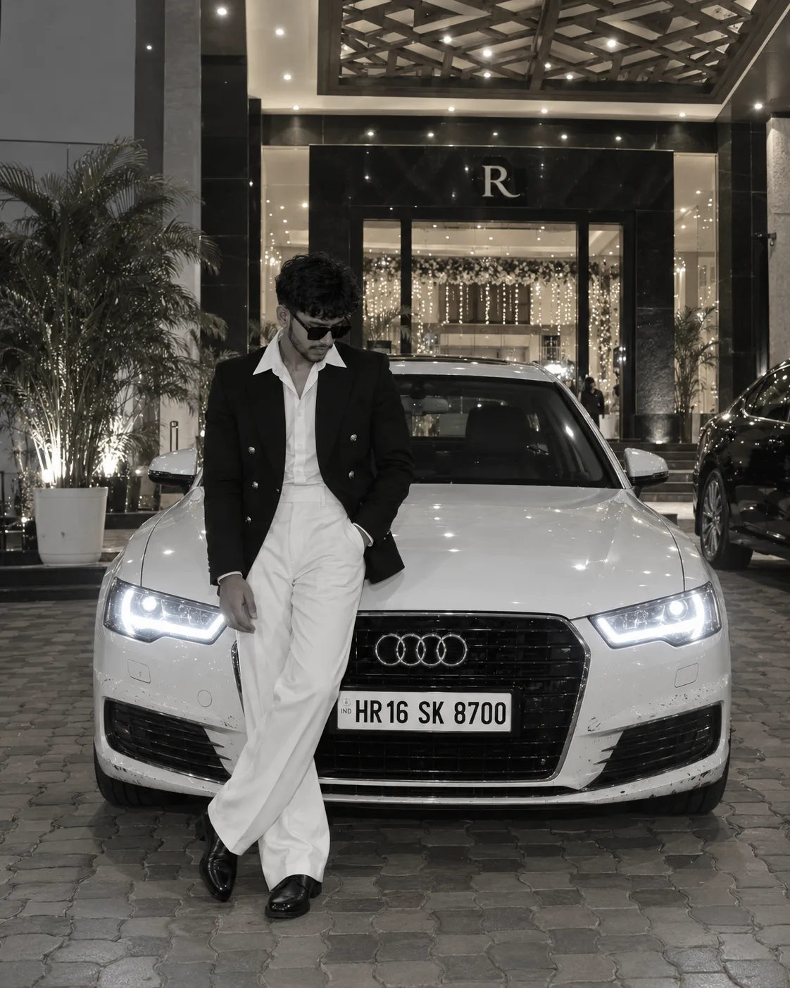 Black and white picture Photorealistic full-body night photo of a young South Asian stylish man in his mid-20s leaning casually against the