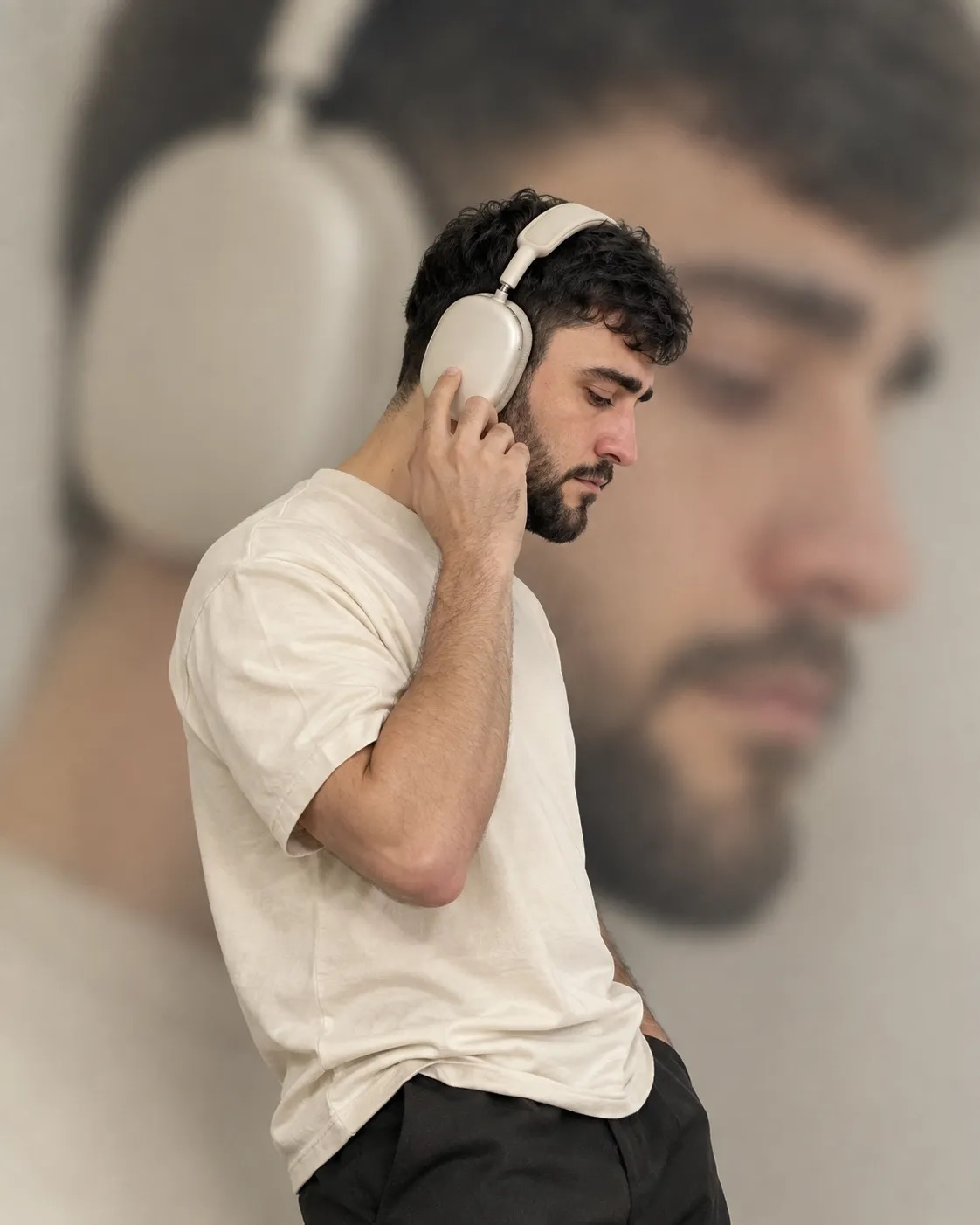 Create a vertical 4:5 photograph of the man from the reference image wearing large ivory-colored headphones, a cream-colored T-shirt, and