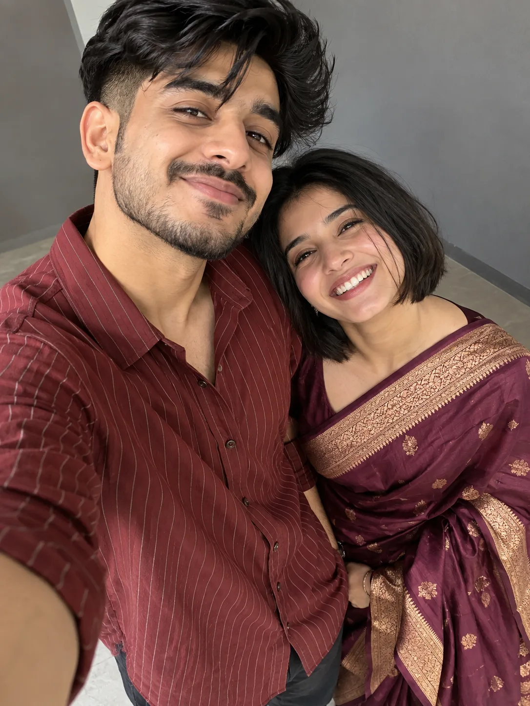 A hyper-realistic, high-angle candid selfie of a joyful South Asian couple smiling brightly.