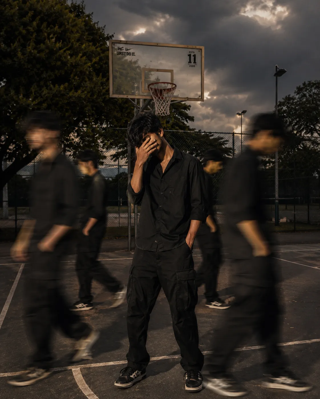 A cinematic streetwear photoshoot of a teenage boy standing on an outdoor basketball court, don't change out fit, face,, head slightly down