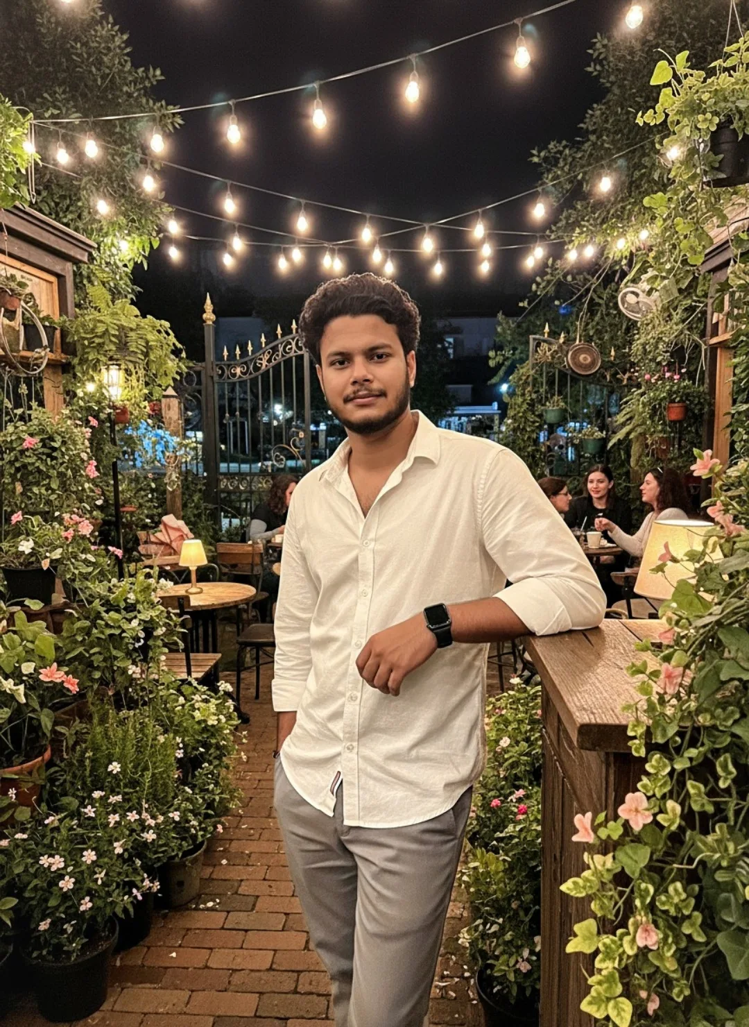 Prompt: A young South Asian man with curly dark hair, light beard and mustache, standing confidently in a lush outdoor cafe garden at