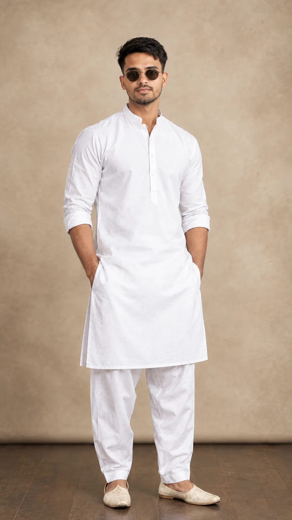 A photorealistic full-body fashion portrait of a handsome adult South Asian man standing confidently in a minimalist indoor studio setting.