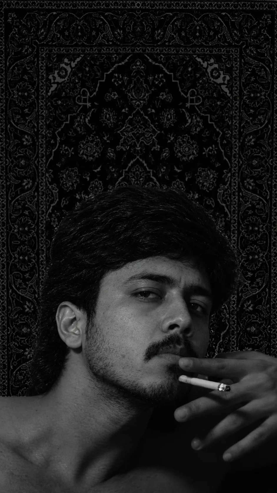 Create an ultra-photorealistic cinematic black-and-white portrait of a young South Asian man in a moody, intimate close-up.