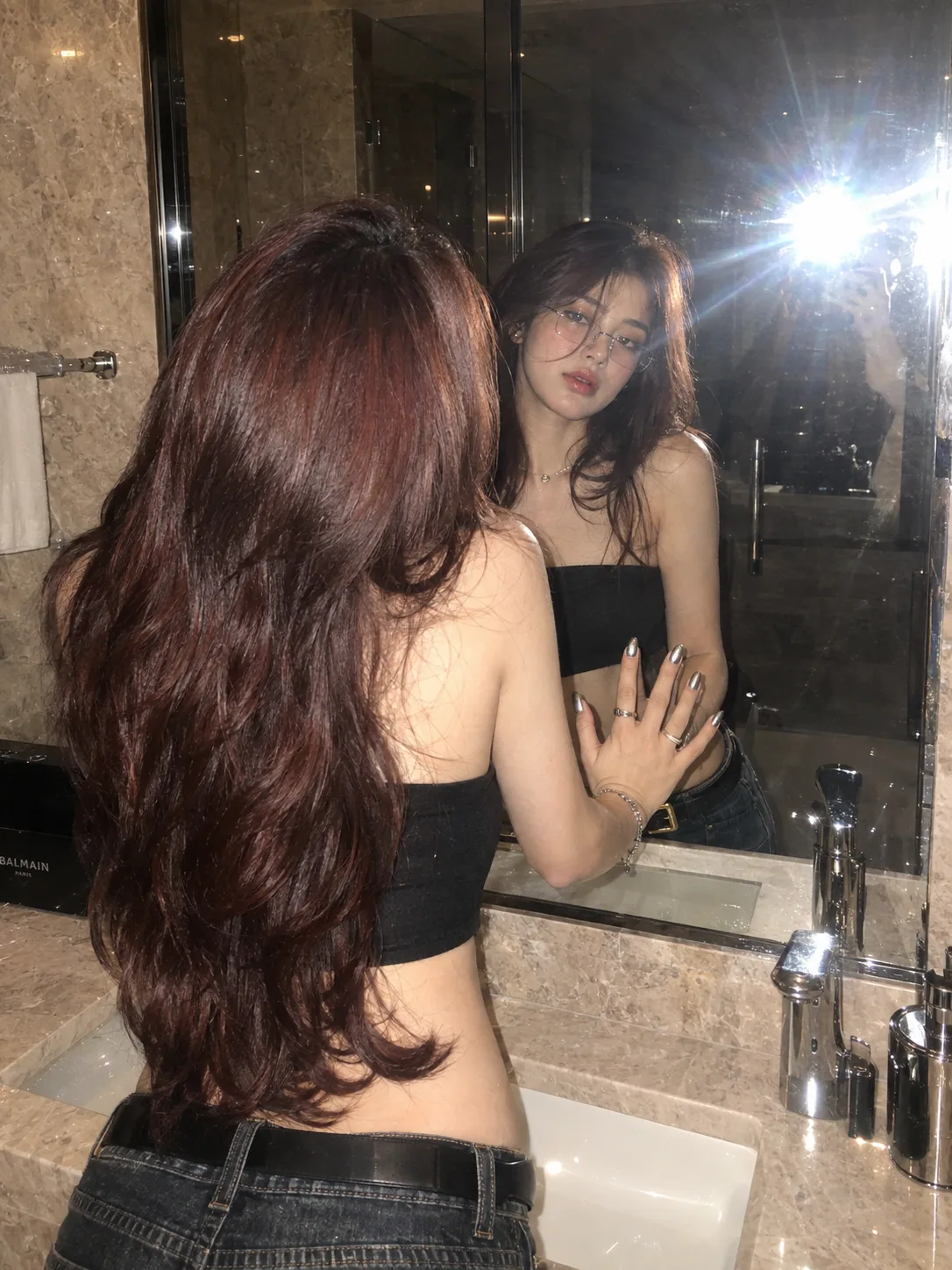 Prompt: A hyper-realistic mirror selfie of a beautiful young woman in a luxurious beige marble bathroom at night, photographed with an