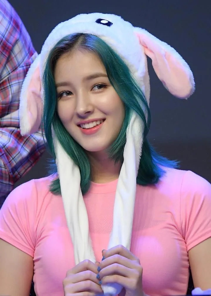 A photorealistic young East Asian woman smiling brightly at the camera, wearing a soft pastel-pink fitted T-shirt and a fluffy white