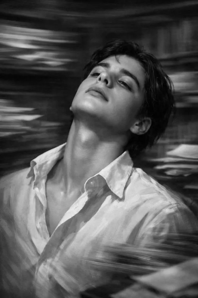 A dramatic black and white portrait of a handsome young man with his head tilted back, looking upwards with an exhausted or dreamy