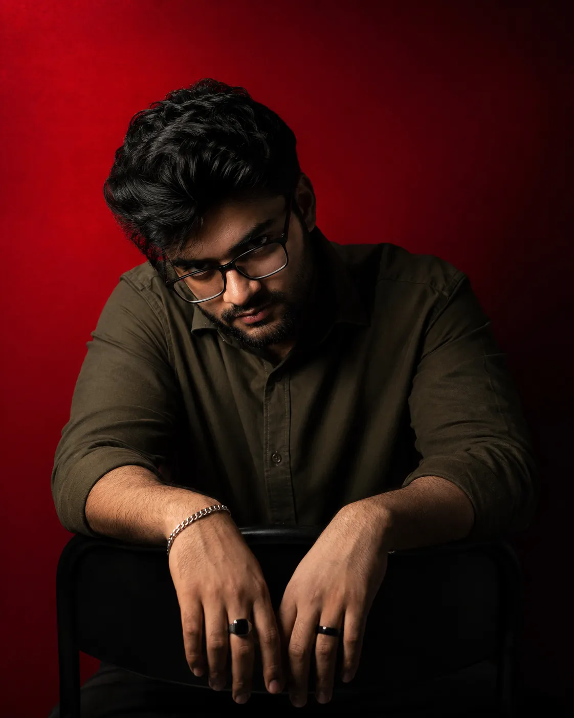 dramatic, high-contrast studlo portrait of a man with dark messy hair and a well groomed beard, wearing black rectangular glasses and a
