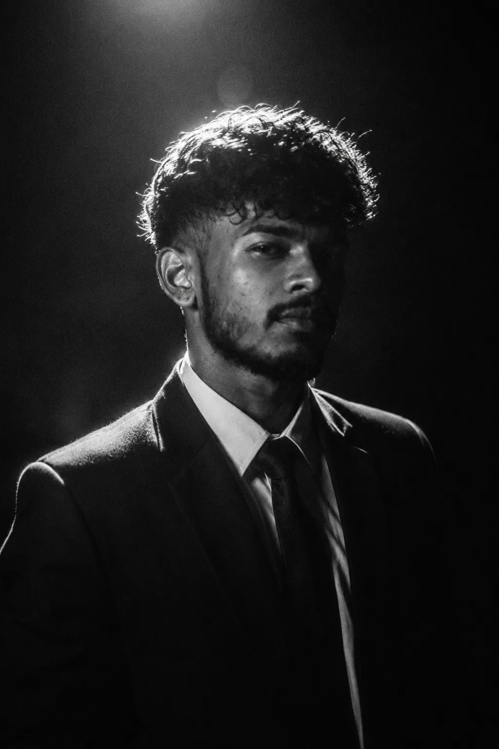Create an ultra-realistic cinematic black-and-white portrait of a confident young man wearing a perfectly tailored black suit, crisp white