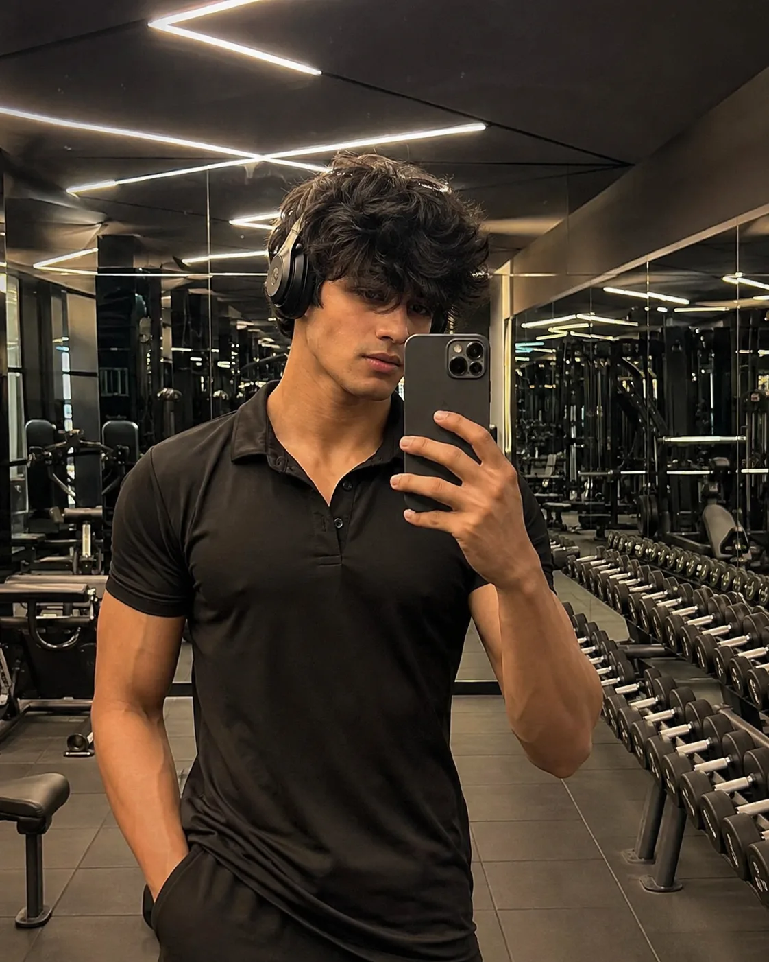 A breathtakingly handsome young male fitness model taking a mirror selfie inside an ultra-modern luxury gym.