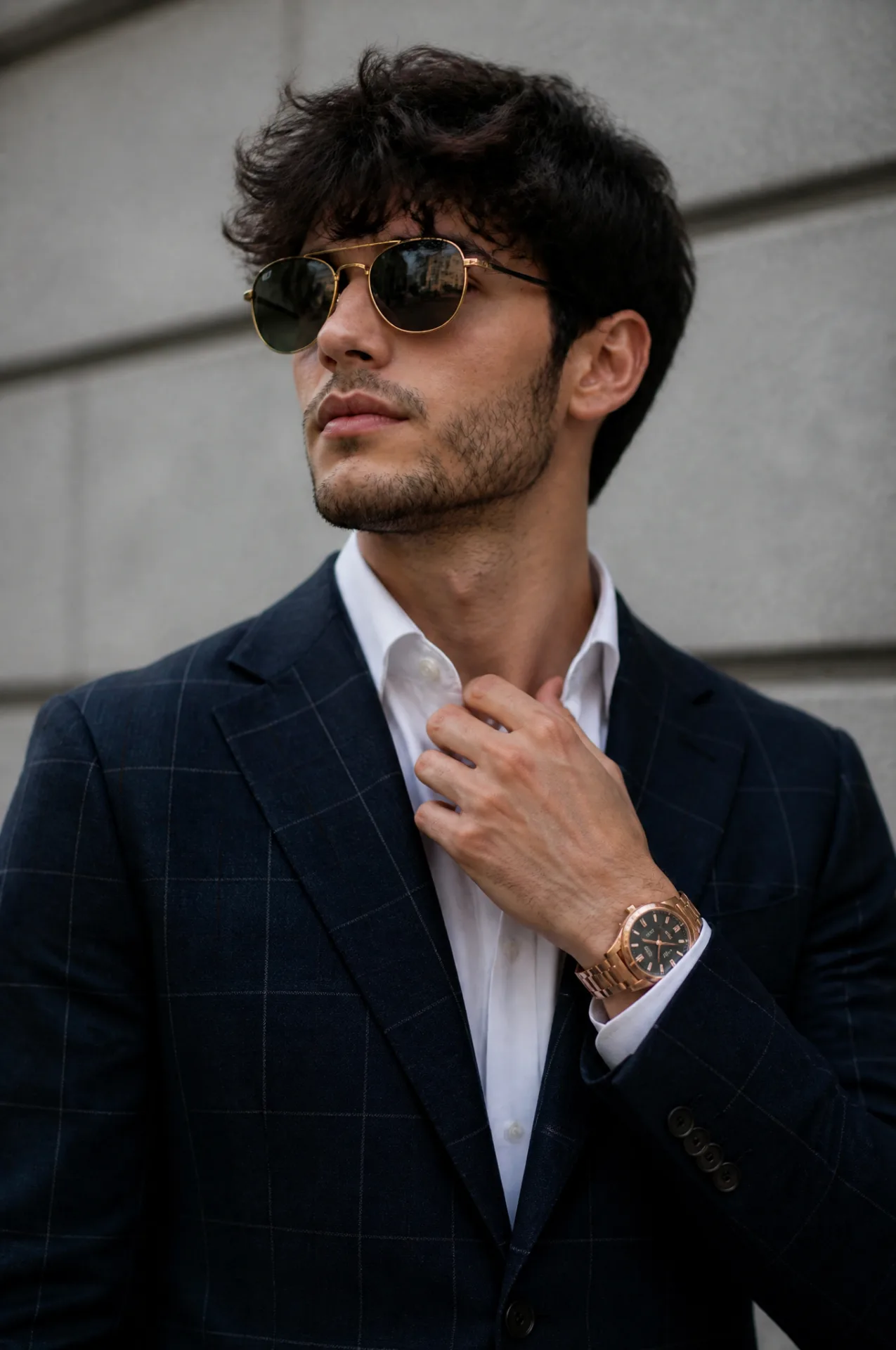 A young man with dark, textured hair and light stubble is captured in a medium shot, adjusting his crisp white shirt collar while wearing a