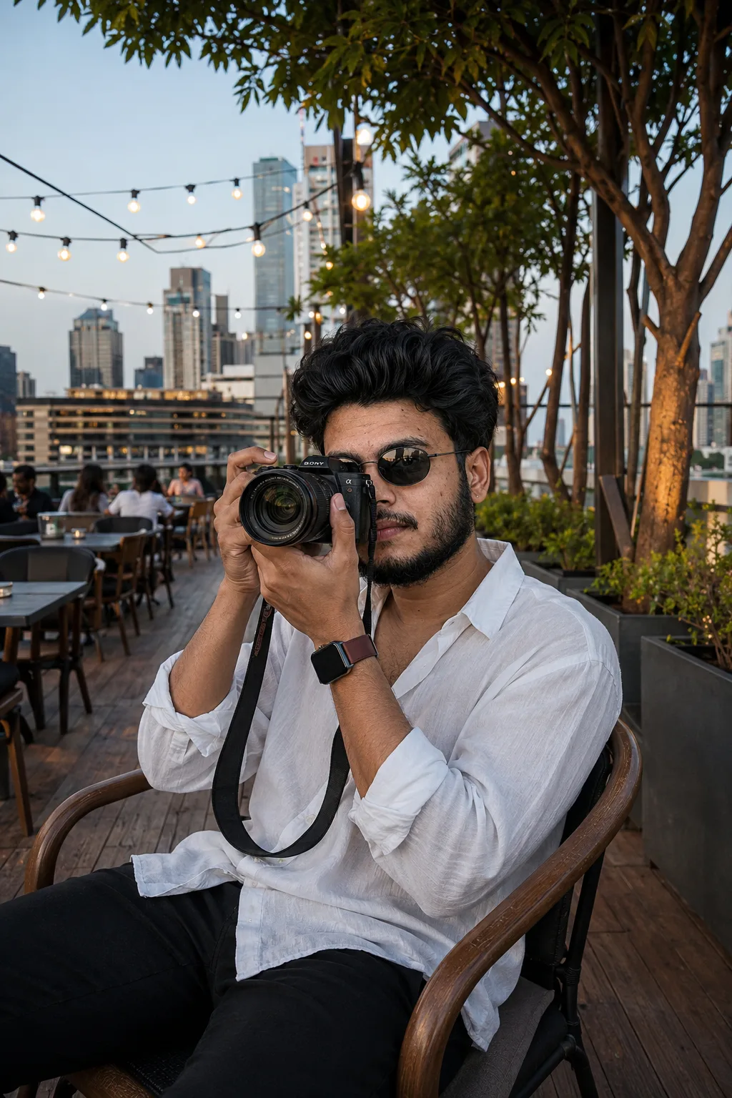 Create an ultra-realistic, premium editorial lifestyle photograph of a stylish young male photographer sitting casually at an elegant