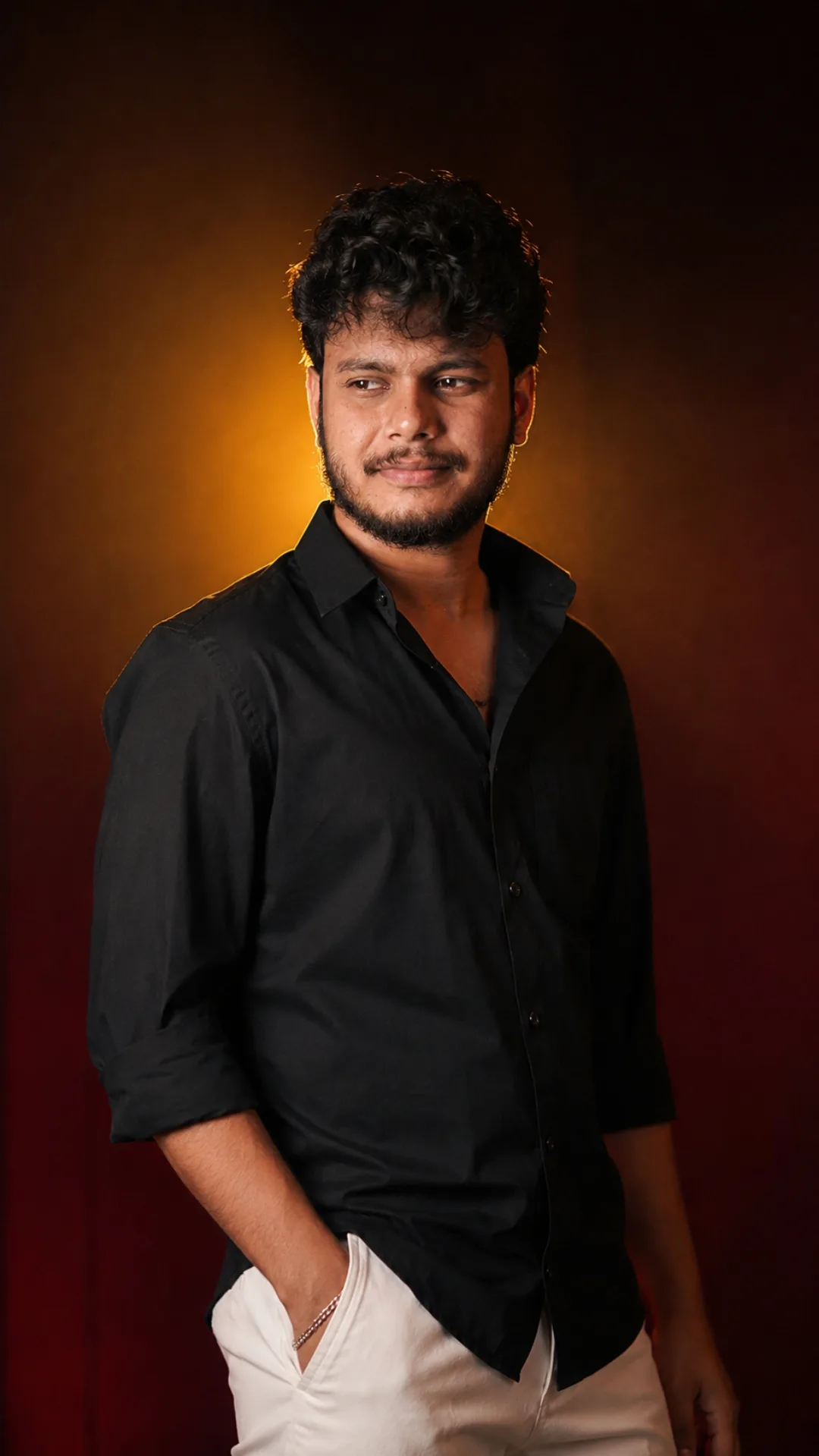 A professional studio portrait of a 26-year-old South Asian male with short, textured curly hair, expressive dark eyes, and a well-groomed