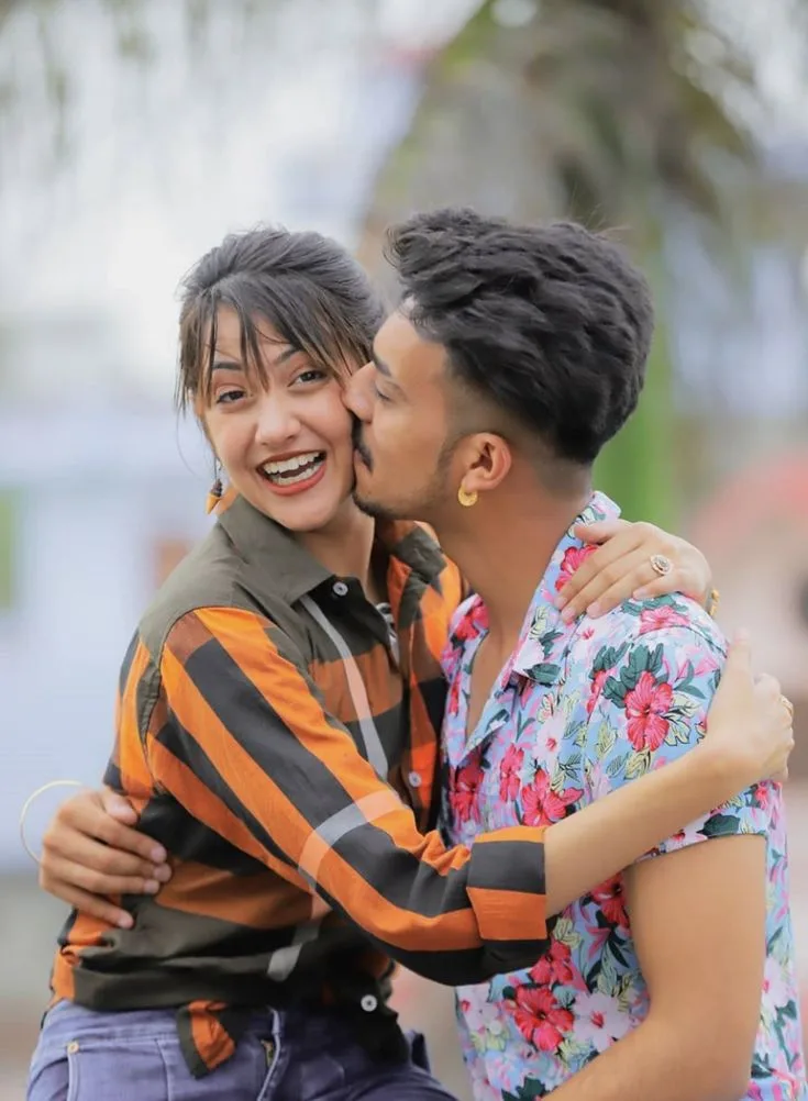 A photorealistic vertical medium shot capturing a candid outdoor moment of the young South Asian couple from the reference image,