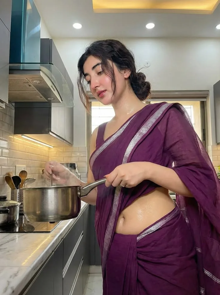 Ultra-realistic photorealistic portrait of a young Indian woman standing naturally in a modern, elegant home kitchen, wearing a rich