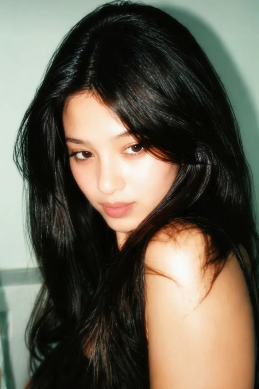 Create an ultra-realistic portrait of a young woman with long, voluminous dark black hair, side-swept strands partially covering her face,