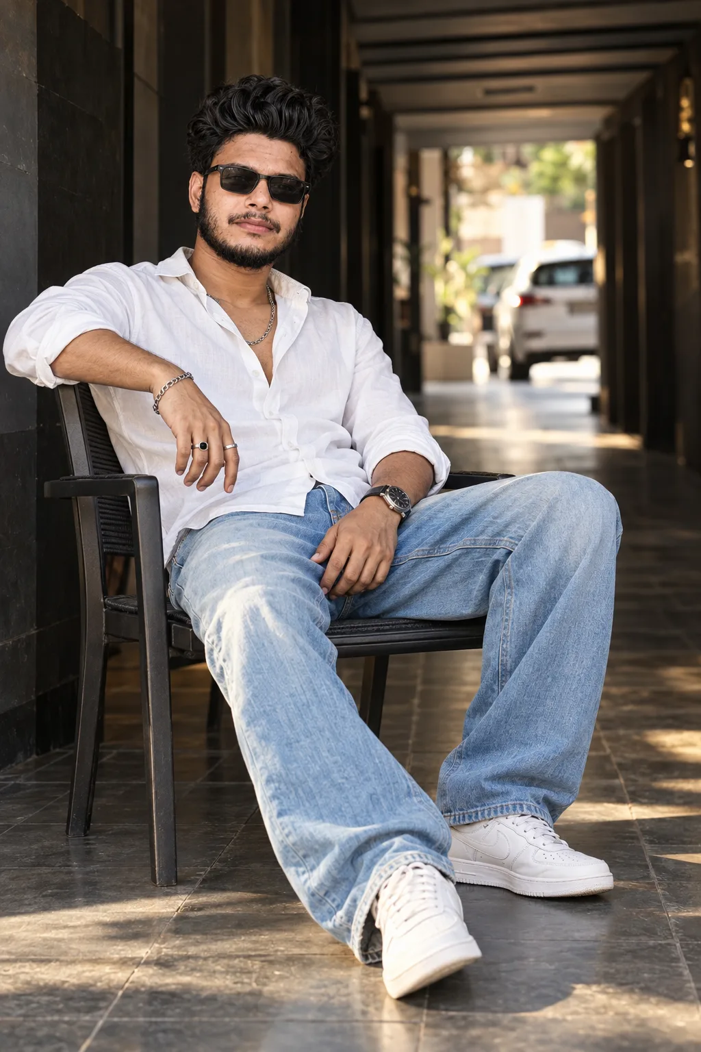 Create an ultra-realistic, premium cinematic lifestyle photograph of a stylish young Indian man relaxing confidently in a black modern