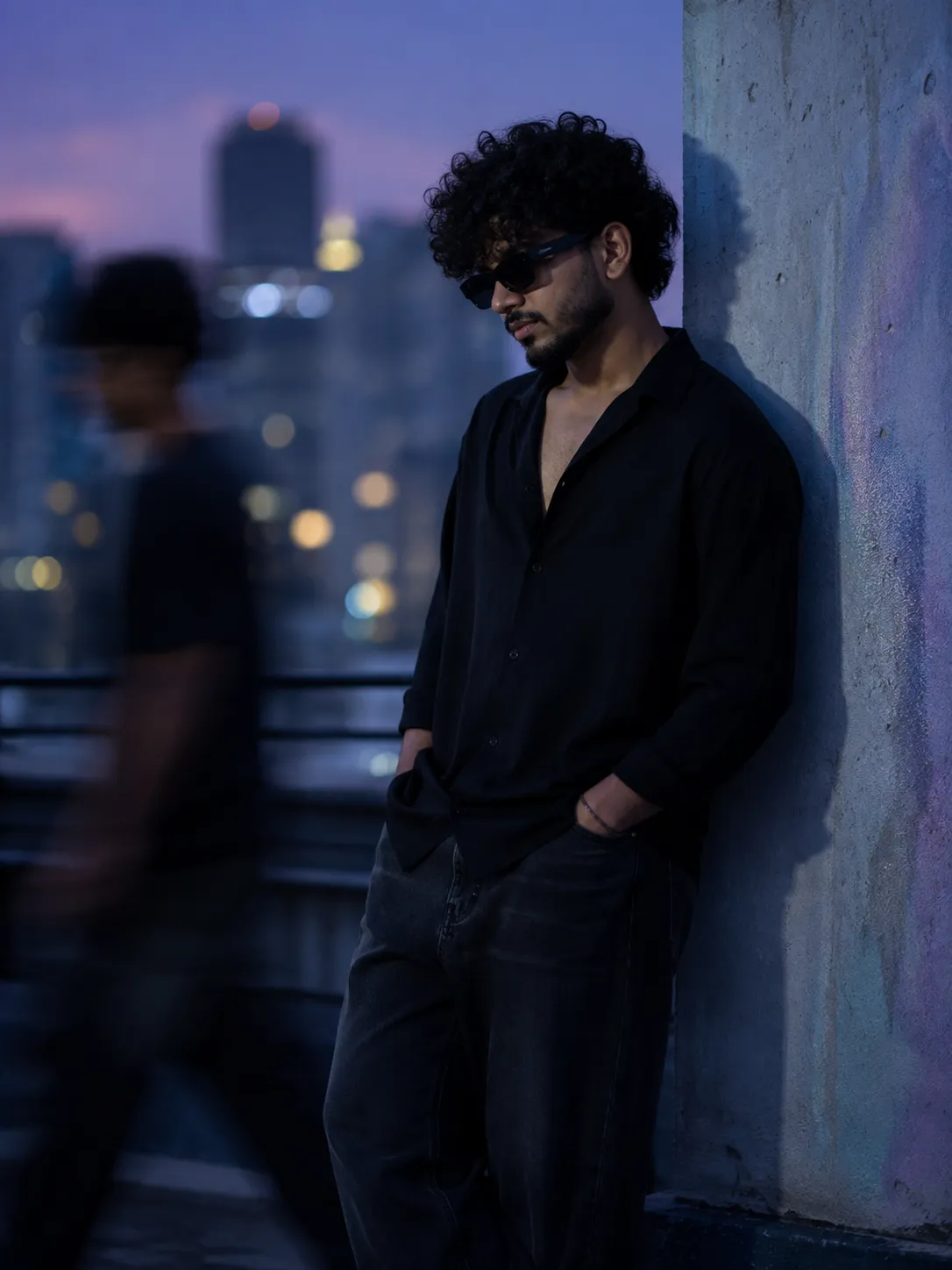 A premium cinematic editorial portrait of a young man leaning against a concrete wall on a rooftop during blue hour.