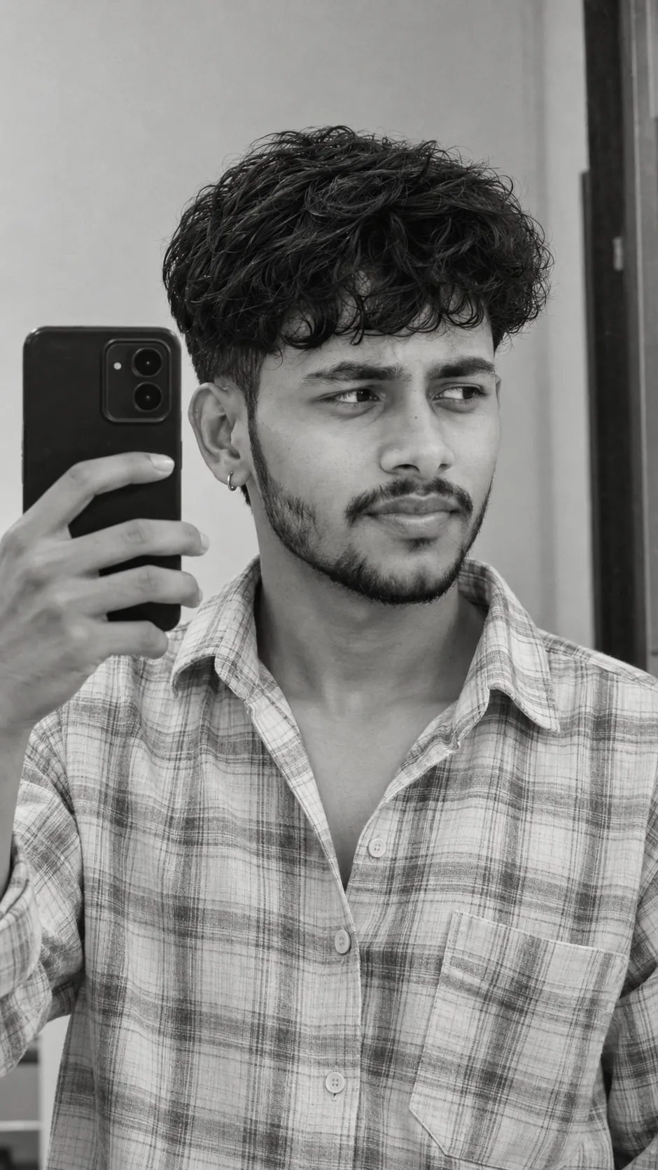 Ultra-realistic professional DSLR photograph of a young South Asian man taking a close-up mirror selfie indoors, framed vertically from