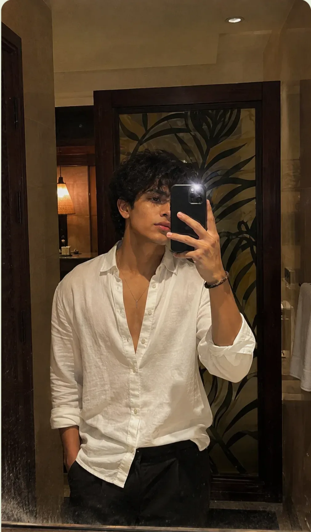 Moody, aesthetic bedroom mirror selfie of a stylish young man holding a sleek black smartphone.