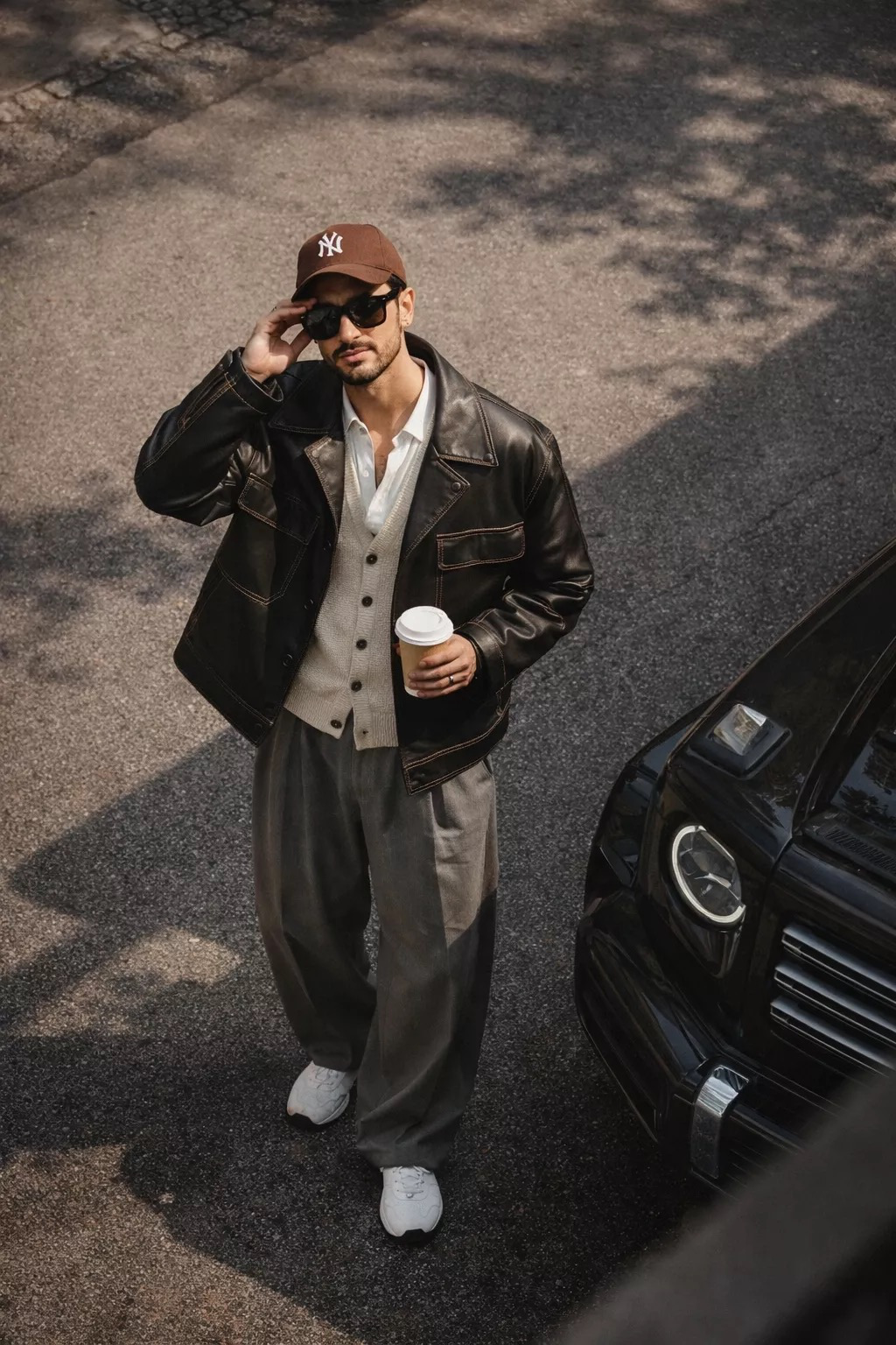 High-angle editorial street-style photograph, taken from a balcony/upper-floor viewpoint looking down at a stylish man standing on sunlit