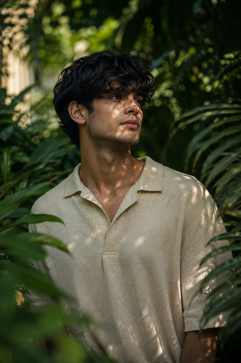 A breathtakingly handsome young male fashion model standing peacefully amidst dense emerald-green foliage in a secluded luxury botanical