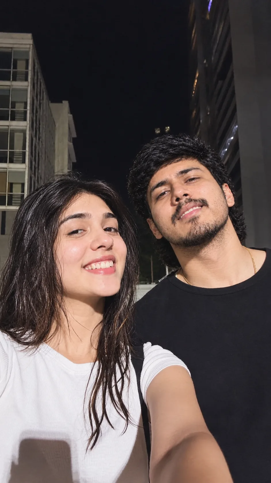 Create a highly realistic nighttime couple selfie featuring the same two people from the reference image.