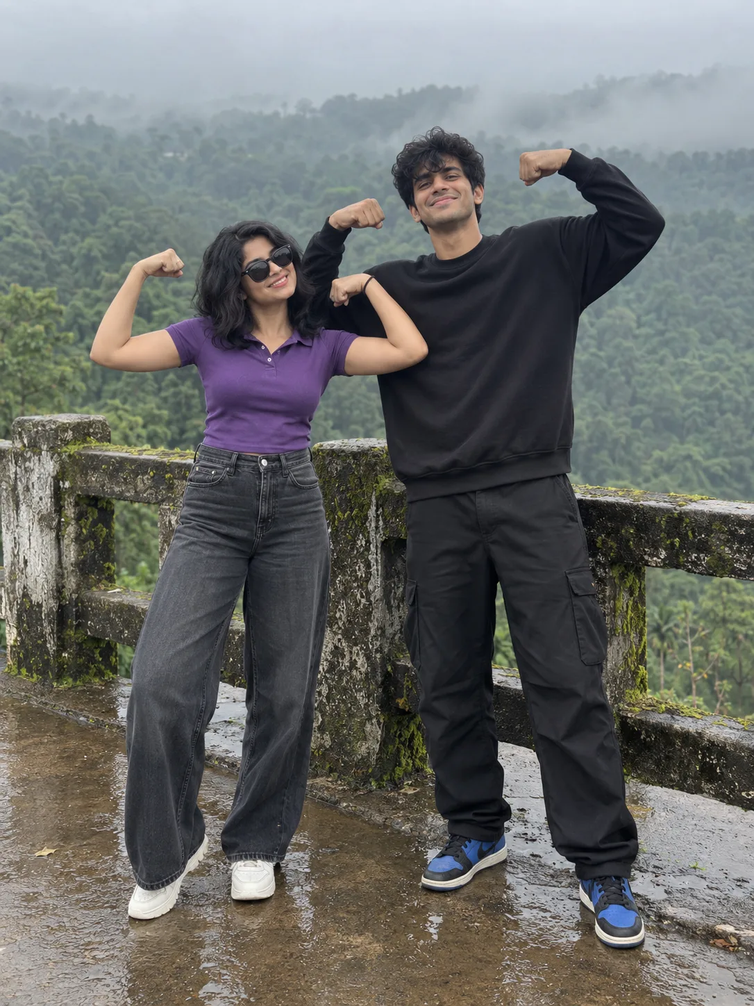 A full-body realistic photograph of a cheerful young Indian couple playfully posing together outdoors.