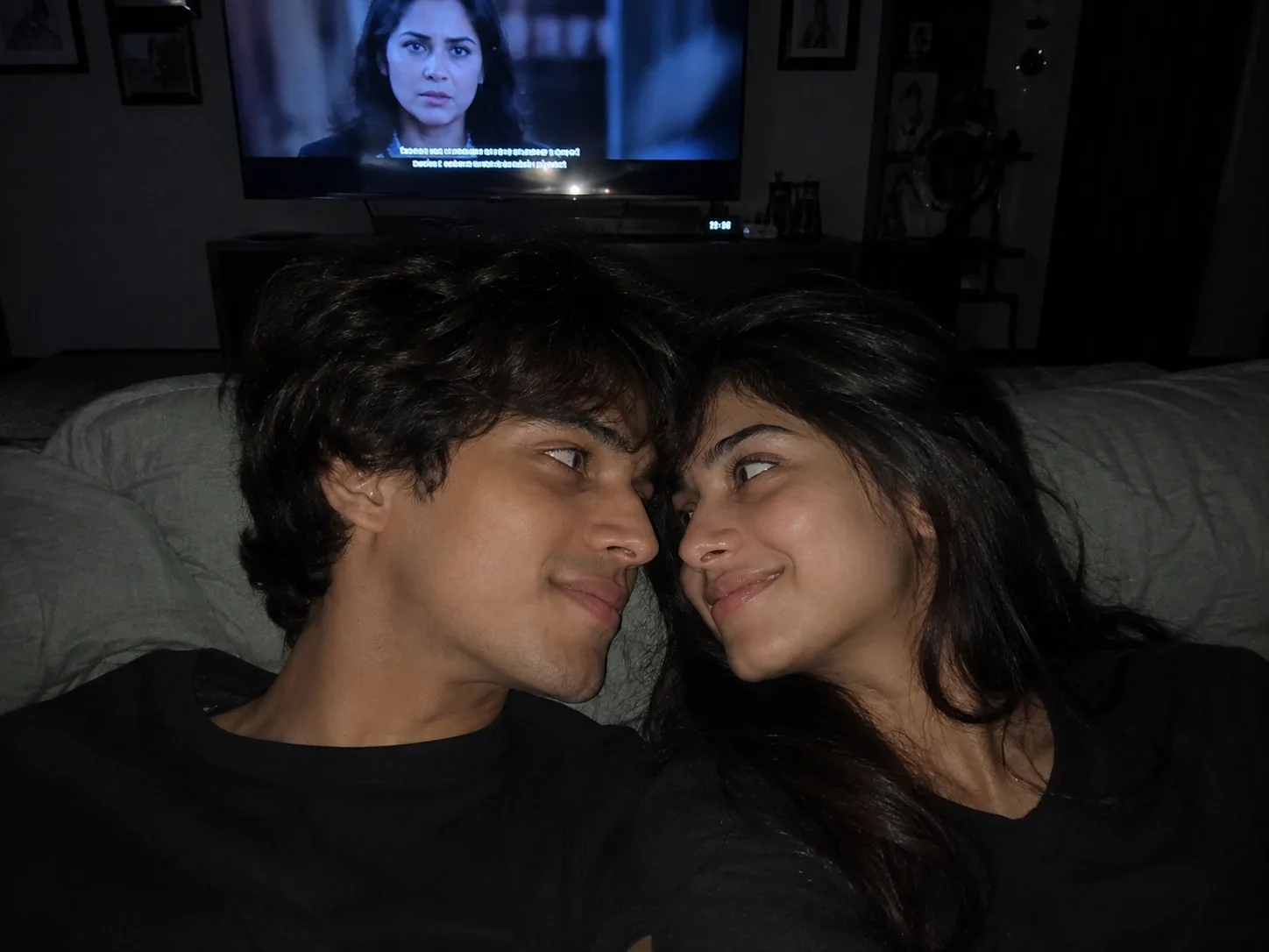 Create an ultra-realistic 8K photograph of a young adult couple who are deeply in love, relaxing together in bed while watching a movie.