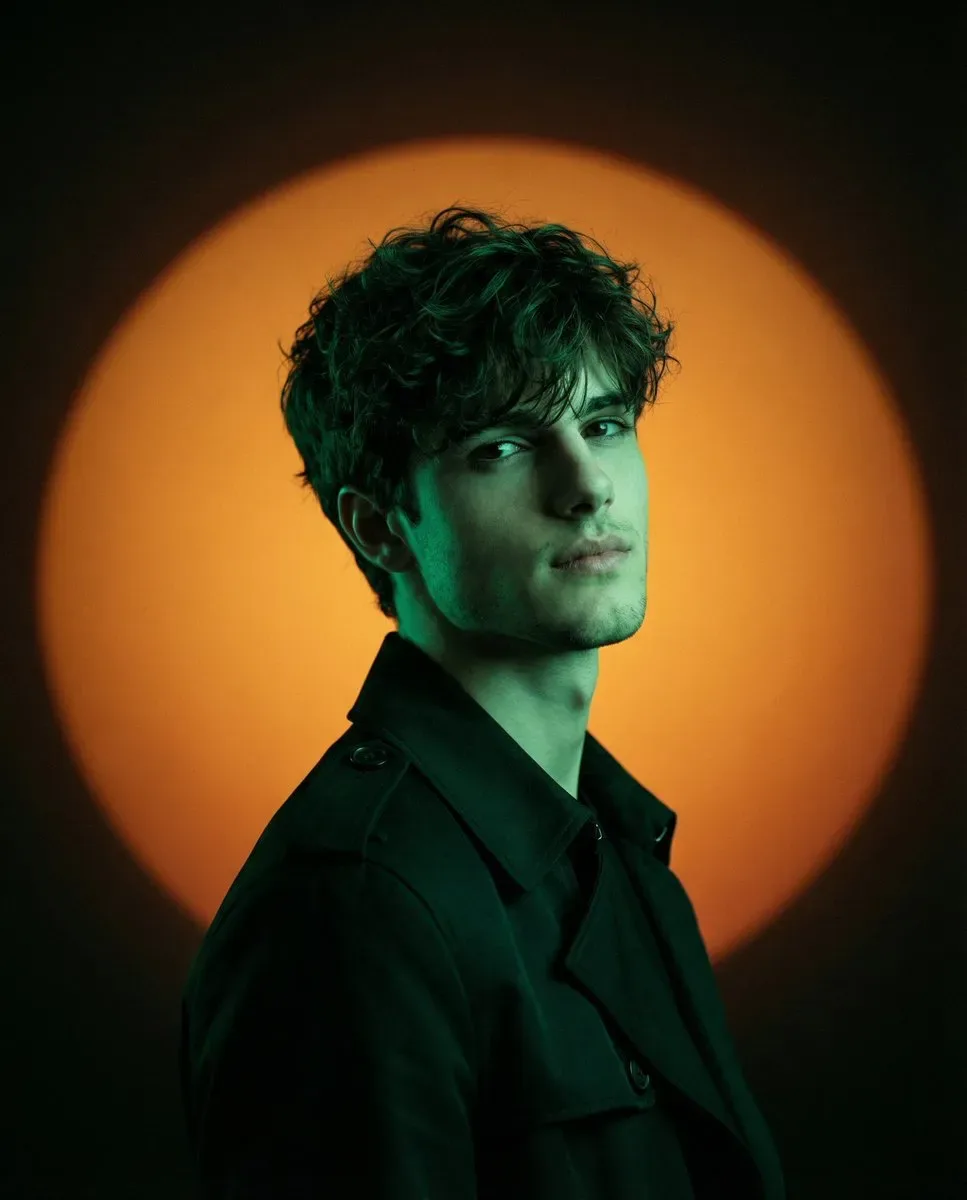 Using a person's photo as the identfy refrence, create a minimalist cinematic fashion-editorial studio portrait with dramatic colored-gel