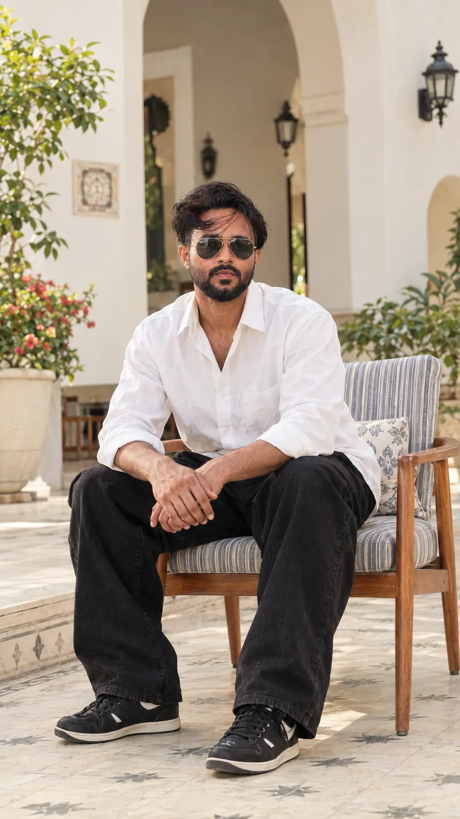Create an ultra-photorealistic high-end cinematic lifestyle fashion photograph of a stylish young South Asian man seated casually on a