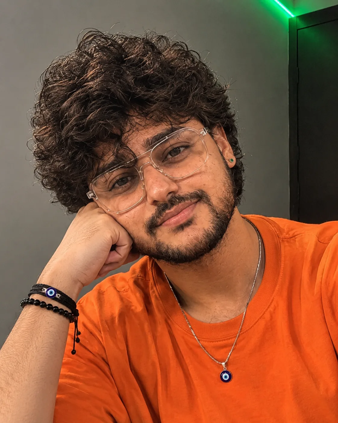 "A close-up selfie-style portrait of a young man with thick, messy, voluminous black curly hair falling loosely across his forehead and