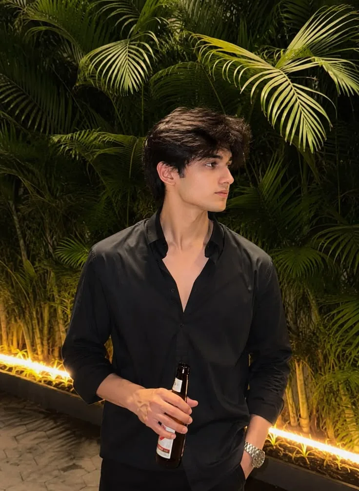 A medium-shot side profile portrait of a handsome 20-year-old South Asian male model with thick, textured messy black hair.