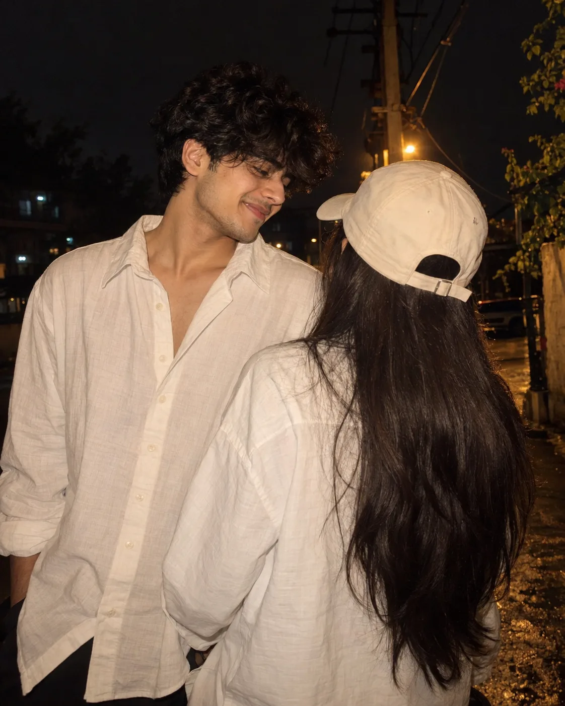 Ultra-realistic cinematic nighttime photograph of a young South Asian couple standing very close together outdoors in a dark setting.
